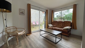 A modern living room with a brown leather sofa, a wooden coffee table, and a wicker chair. - Maison de campagne, Sainte Mère Église, site historique (Sainte-Mère-Eglise)