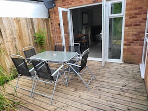 A patio with a glass table and chairs, a wooden deck, and a brick wall.