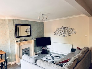 A living room with a fireplace, a sofa, a TV, and a decorative tree wall art.