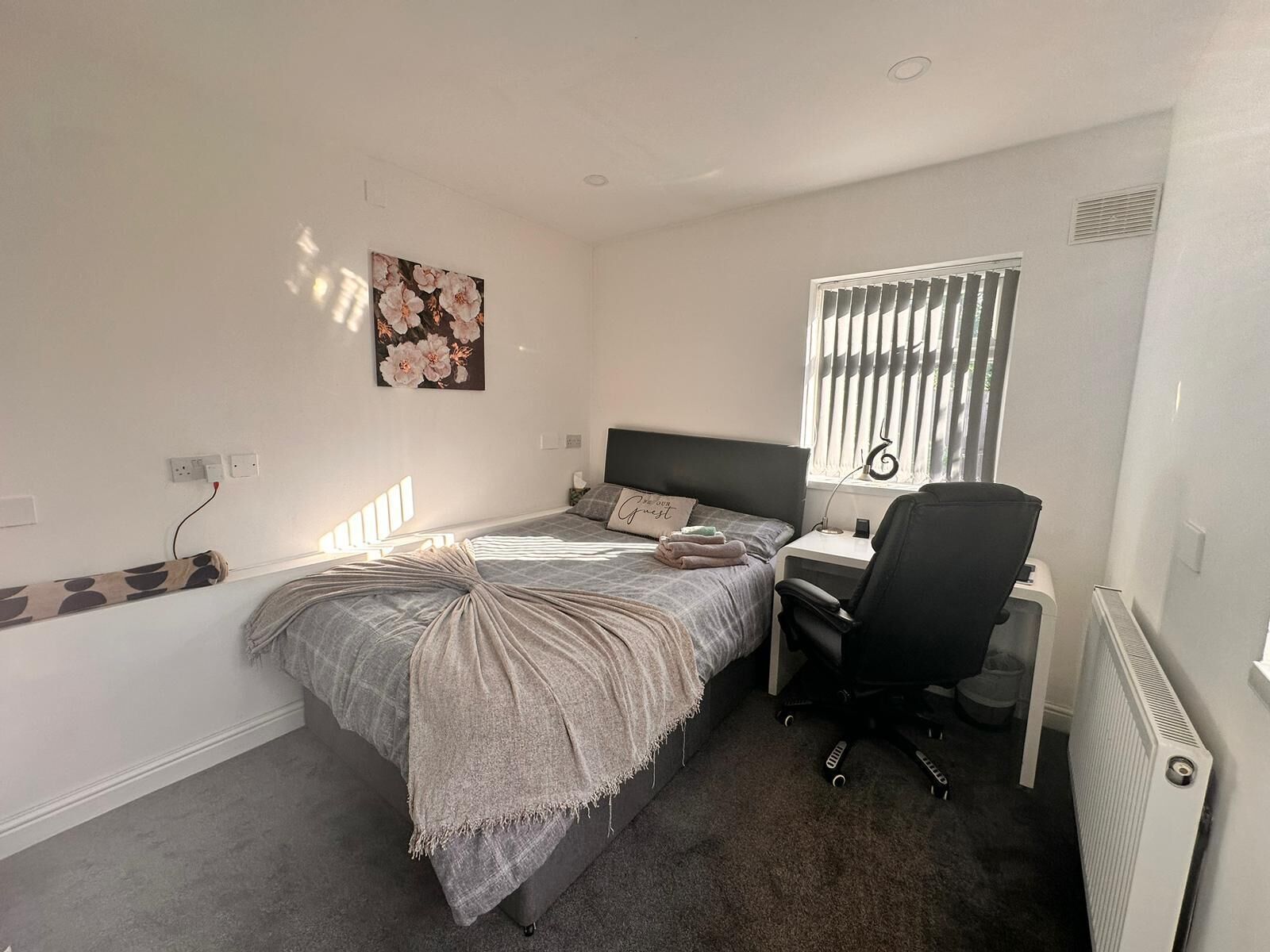 Un dormitorio con cama, escritorio, silla, radiador y ventana con persianas.