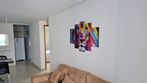 Una sala de estar con un sofá beige, una cocina al fondo y un cuadro abstracto de colores en la pared.