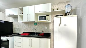 Una cocina con armarios blancos, microondas, licuadora, refrigerador y estufa.