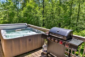 Ein Whirlpool und ein Grill auf einer Holzdiele mit Wald im Hintergrund.