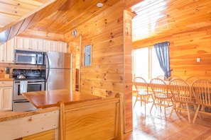 Ein Holzblockhaus-Interieur mit Küche, Essbereich und einem großen Fenster mit Vorhängen.