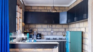 Eine Küche mit dunklen Schränken, einem türkisblauen Kühlschrank und einer Backsteinwand.