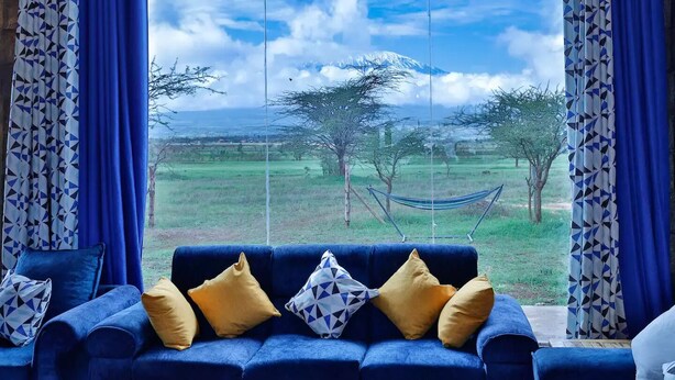 Ein blaues Sofa mit gelben und gemusterten Kissen, eine Hängematte und Blick auf ein grasbewachsenes Feld mit Bäumen und einem Berg im Hintergrund.