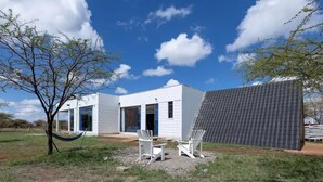 Ein modernes Haus mit weißer Fassade, einer überdachten Terrasse mit zwei weißen Adirondack-Stühlen und einer Hängematte.