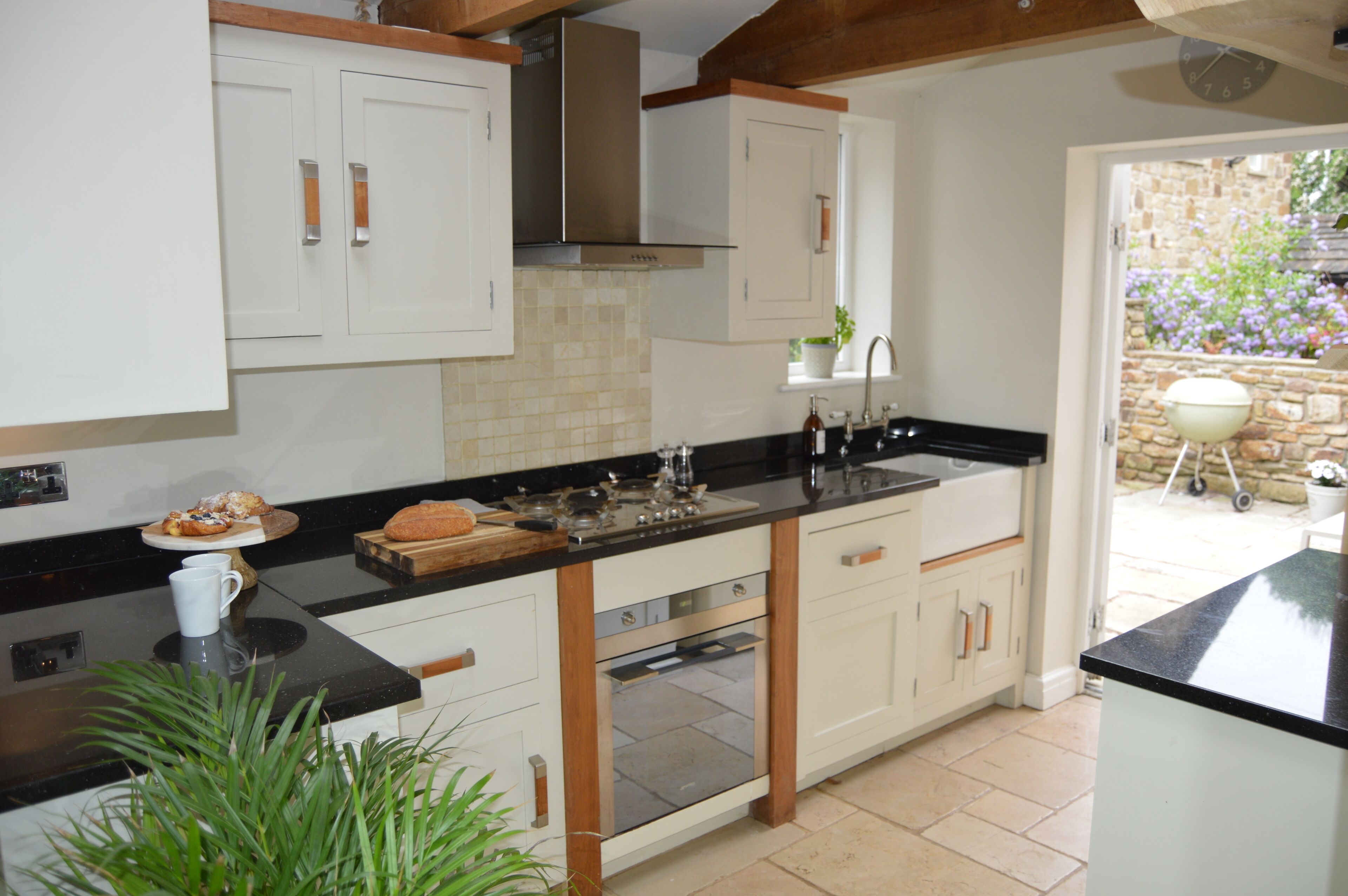 A modern kitchen with white cabinets, a black countertop, and a built-in oven. There is a window with a view of a garden.