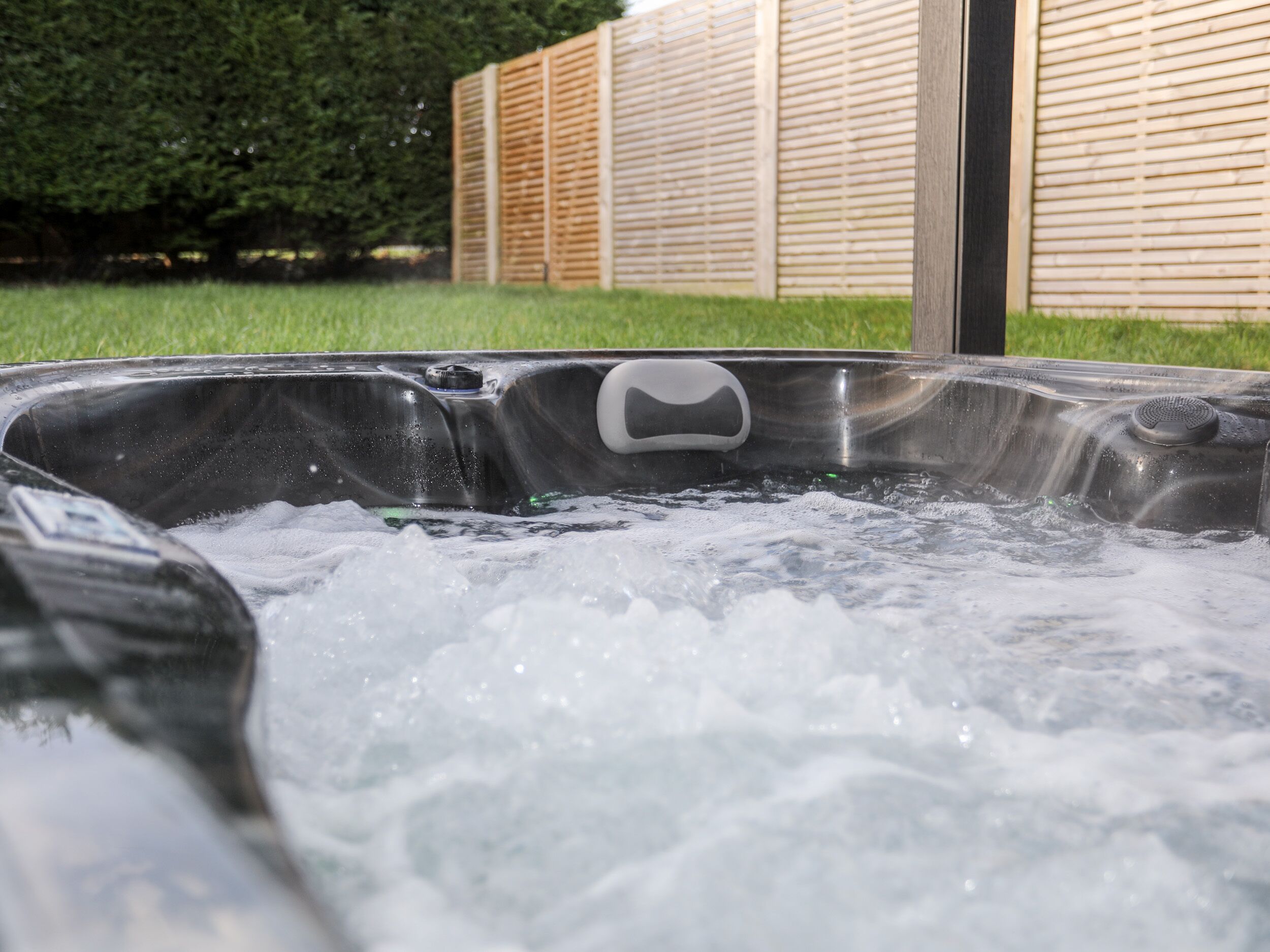 A hot tub with a control panel, surrounded by a wooden fence and a grassy area.