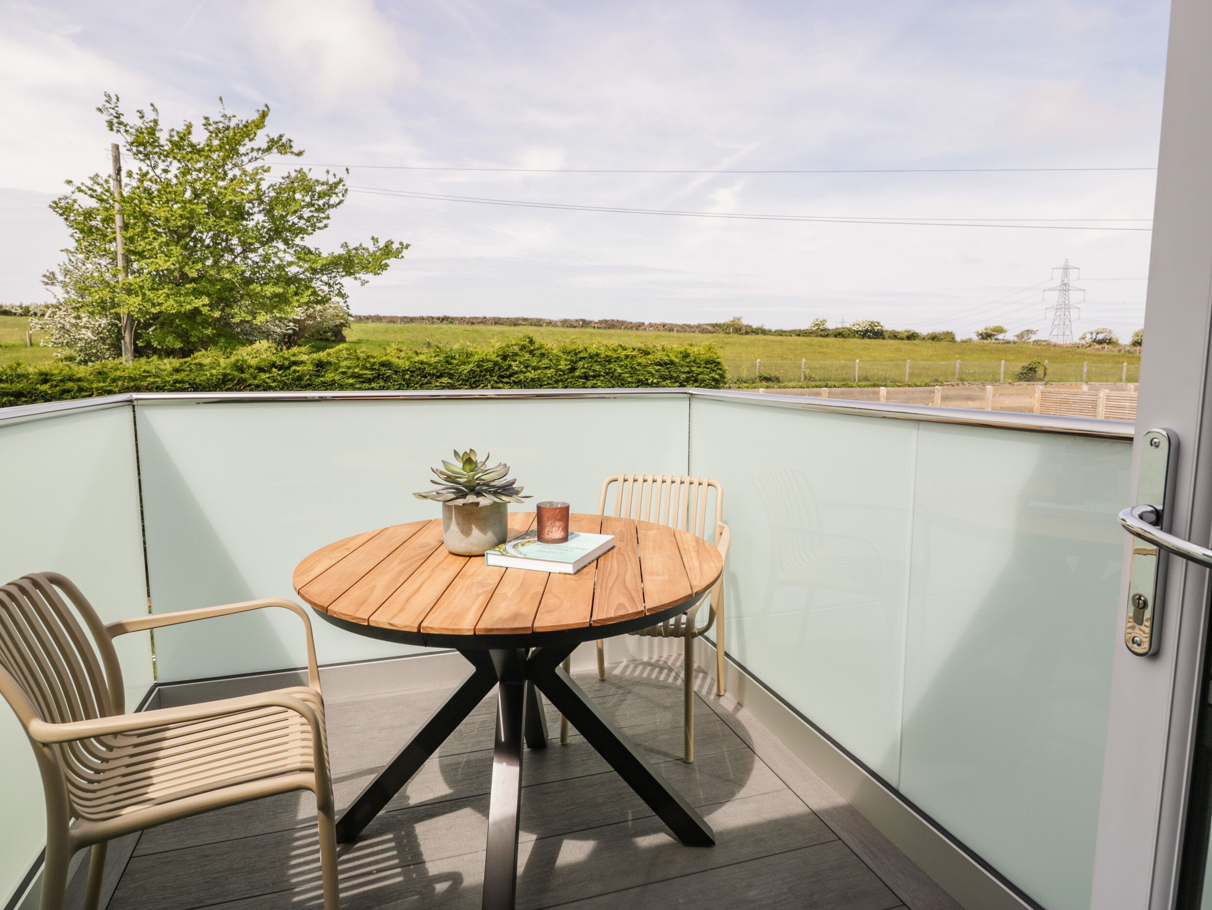 Un balcon avec une table et des chaises en bois, une plante en pot et un livre.