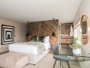 Une chambre moderne avec un mur en bois à motifs en chevrons, un grand lit avec une literie blanche, une table en verre avec une chaise et un miroir sur le mur.