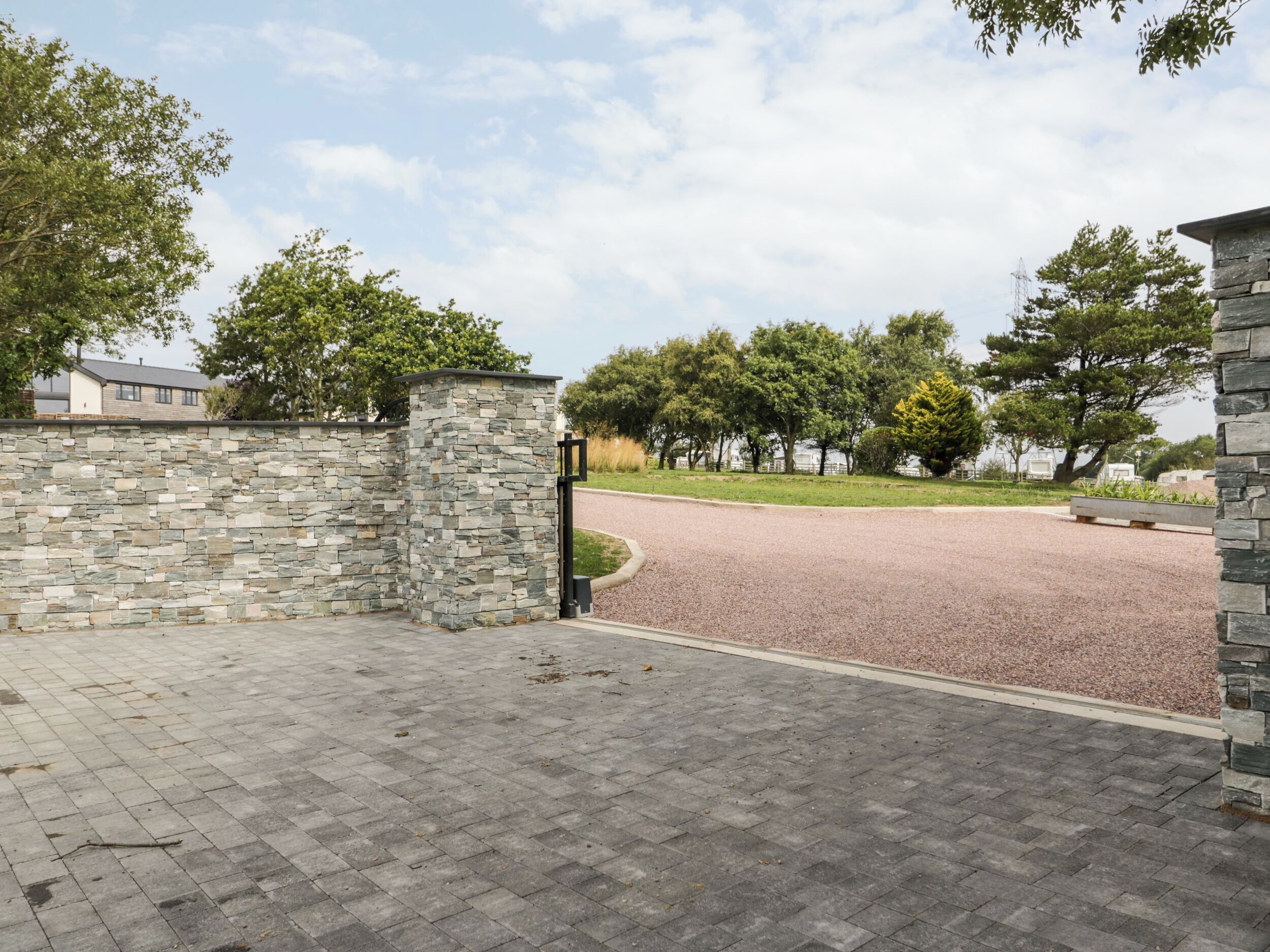 A paved driveway leading to a stone wall with a gate.