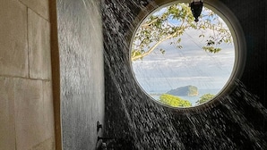 A circular window with a view of a landscape, a textured wall, and a hanging light fixture. - 6BR Luxury Ocean View Villa • Infinity Pool • Private Cinema • Spa (Quepos)