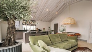 Una sala de estar moderna con un sofá verde, una maceta grande con un árbol y una zona de comedor con una lámpara colgante.