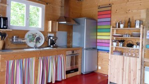 A compact kitchen with wooden walls, a stainless steel refrigerator, a microwave, and a coffee maker.