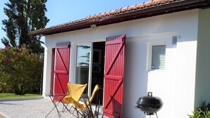 A house with red shutters, a yellow folding chair, and a barbecue grill outside.