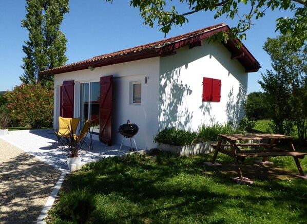 A white building with a red roof, a barbecue grill, and a wooden deck. - Ressourcez-vous en Béarn Dans un Gîte au Contact de la Nature (Ramous)
