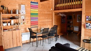 A wooden cabin interior with a dining area, kitchen, and a loft space.