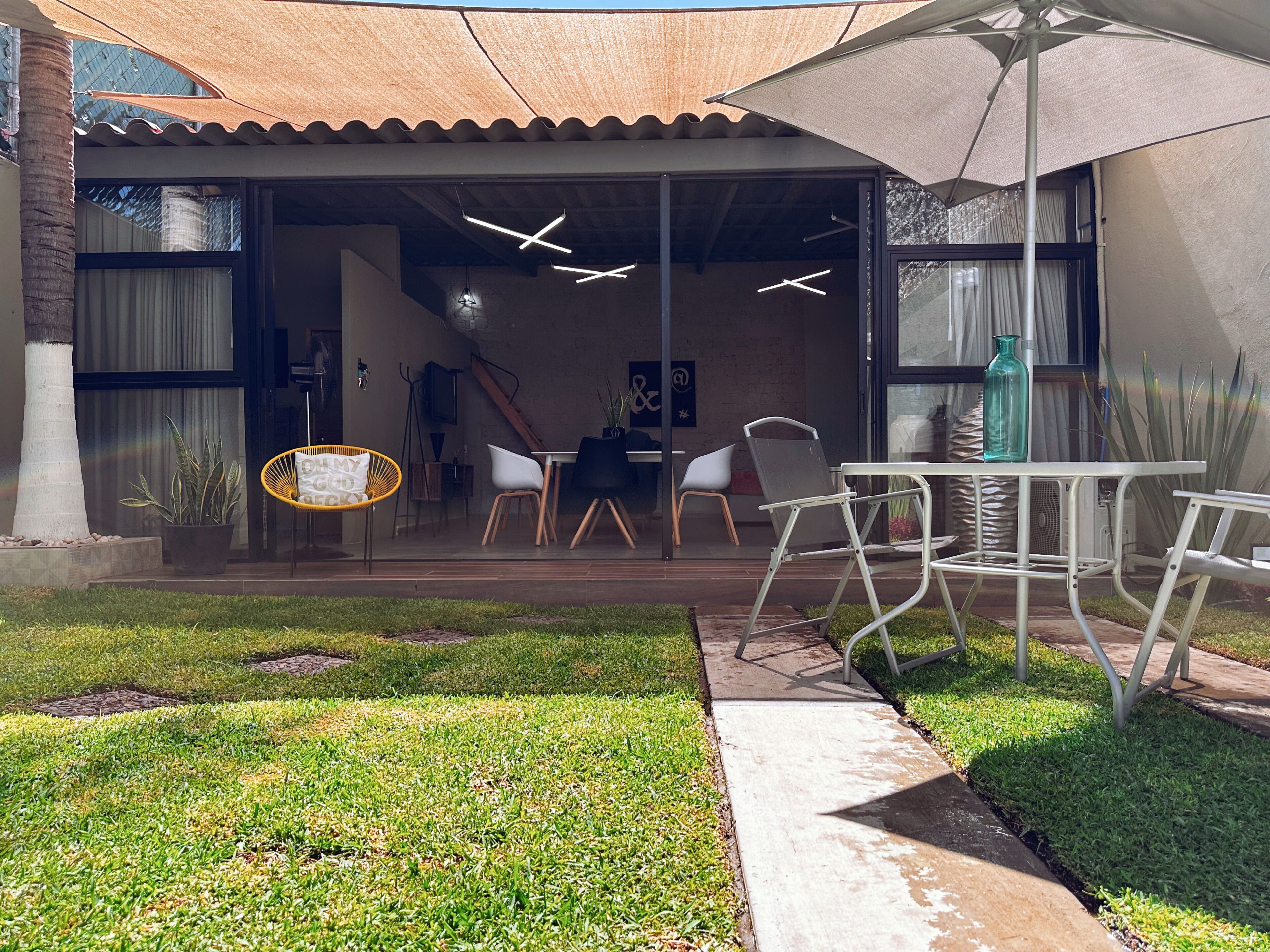 Un espace extérieur aménagé en terrasse, avec une table et des chaises, un pot de fleurs et un grand parasol pour faire de l’ombre.