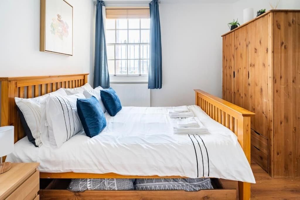 A neatly made bed with white and blue bedding, a wooden headboard, and a wooden wardrobe in a room with a window and curtains.
