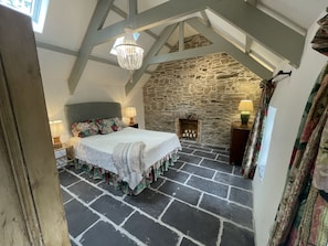 Quarto com lareira de pedra, cama com roupa de cama floral e um candelabro.