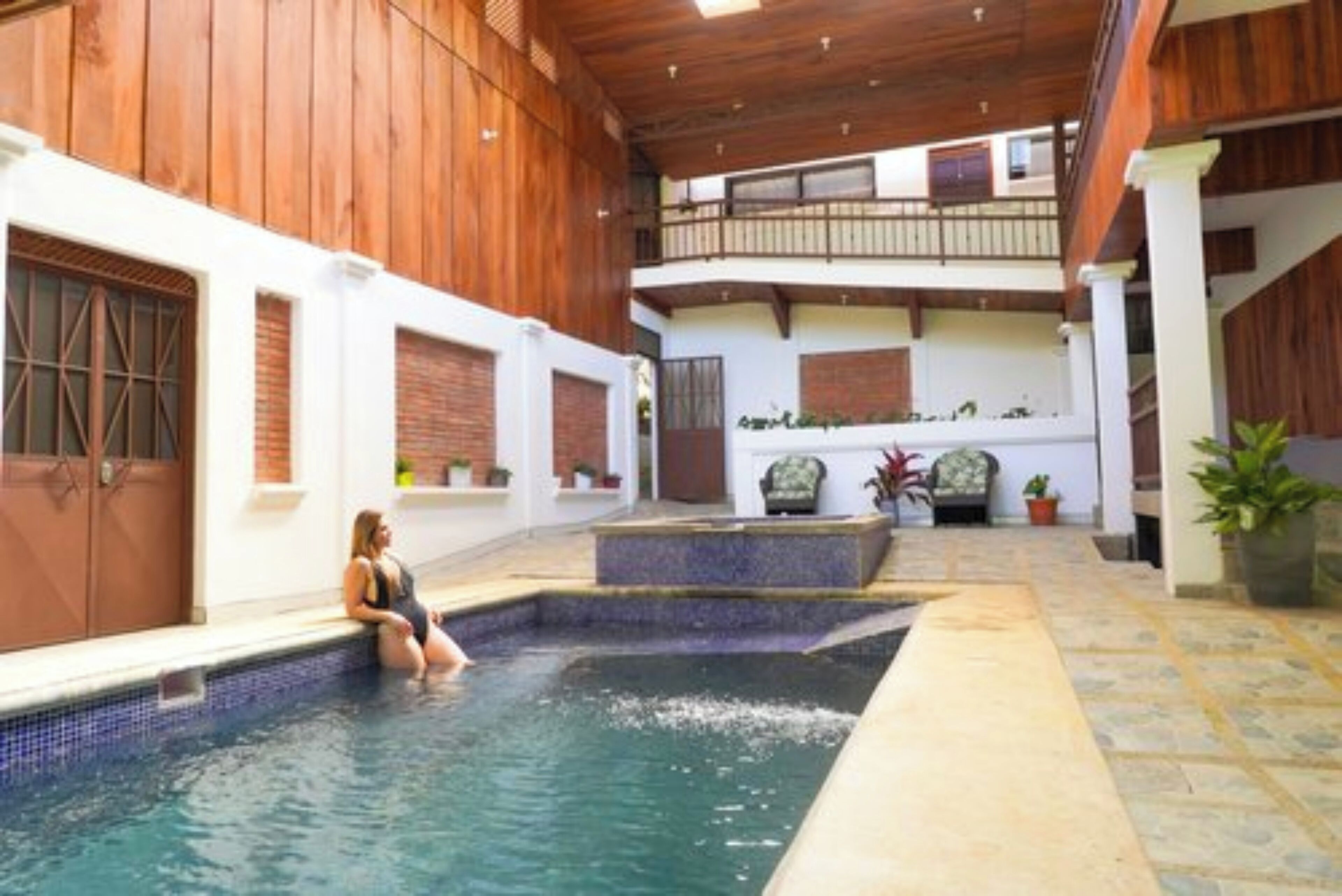 Zona de piscina con una persona sentada en el borde, rodeada de paredes de madera y un suelo de baldosas.