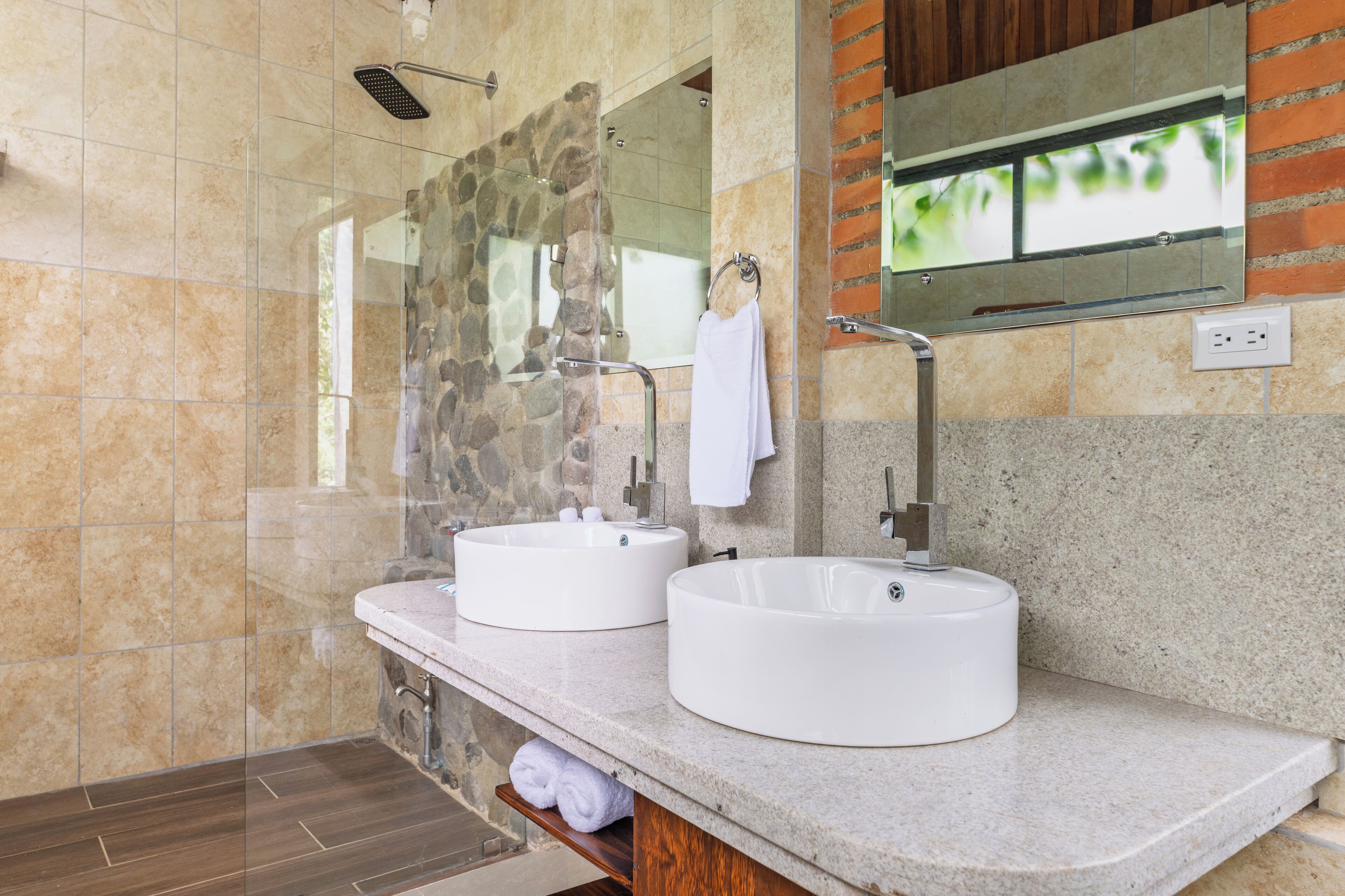 A modern bathroom with two round white sinks, a glass shower enclosure, and a mirror above the sinks.