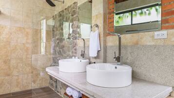 A modern bathroom with two round white sinks, a glass shower enclosure, and a mirror above the sinks.
