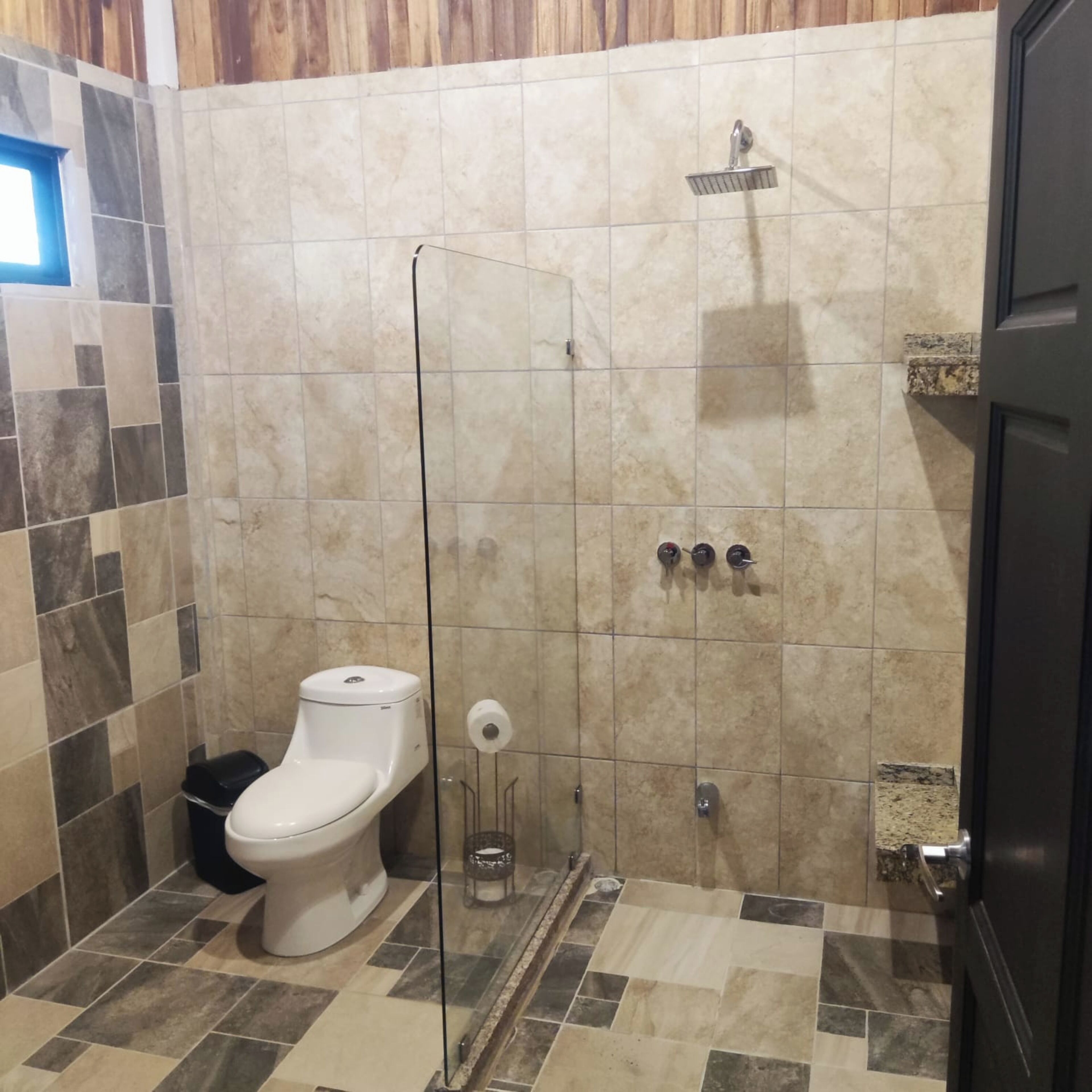 Une salle de bain comprenant des toilettes, un espace douche et un sol carrelé.
