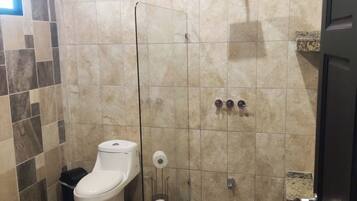Une salle de bain comprenant des toilettes, un espace douche et un sol carrelé.