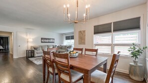 Un espace repas comprenant une table et des chaises en bois, un lustre et une vue sur l’extérieur grâce à de grandes fenêtres.