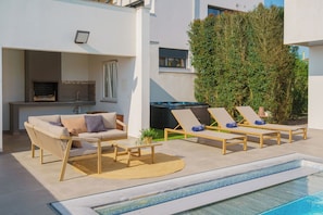 A modern outdoor living area with a pool, lounge chairs, a sofa, and a barbecue grill.