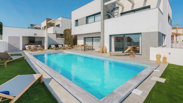 A modern two-story house with a swimming pool, outdoor furniture, and a clear blue sky.