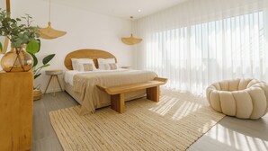 A modern bedroom with a wooden bed, bedside tables, a bench, a round chair, and a large window with sheer curtains.