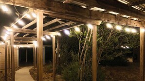 A wooden pergola structure with string lights, surrounded by vegetation and a concrete pathway. - 1 Block From W Main St - Quiet Spacious Getaway (Fredericksburg)