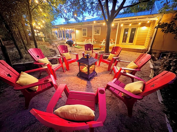 Un espace extérieur aménagé avec des chaises Adirondack rouges disposées autour d’un foyer central.