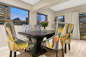 A dining area with a dark wooden table, six upholstered chairs with a colorful geometric pattern, and a vase with pink flowers. - 2 BD Penthouse in the Heart of the Mother City (Cape Town)