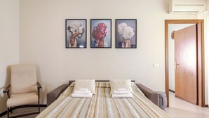 Une chambre d’hôtel avec un lit, une chaise, une porte et trois tableaux encadrés accrochés au mur.