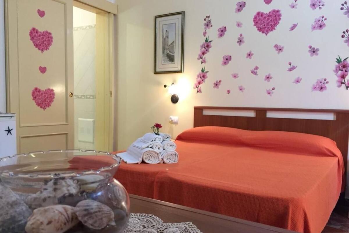 Hotellihuone, jossa on sänky, kukka-aiheisilla tarroilla koristeltu seinä, kehystetty kuva ja pöydällä simpukoiden täyttämä kulho.
