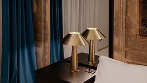 A bedroom with a bed, two bedside lamps, a dark wooden nightstand, and blue curtains.