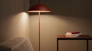 A room with a red floor lamp casting light on a table with books and a framed document on the wall.