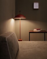 Una stanza con una lampada da terra rossa che illumina un tavolo con libri e un documento incorniciato appeso al muro.