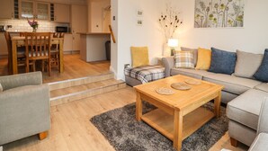 A modern living room with a wooden coffee table, grey sofa, and a dining area with wooden chairs and a small table. - Delabere Road (Cheltenham)