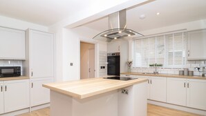 A modern kitchen with white cabinetry, a central island, a microwave, and a built-in oven. - Delabere Road (Cheltenham)