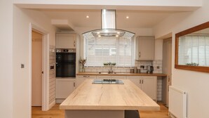 A modern kitchen with a central island, built-in oven, and a large window with blinds. - Delabere Road (Cheltenham)