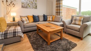 A modern living room with a grey sofa set, a wooden coffee table, and a large window with curtains. - Delabere Road (Cheltenham)