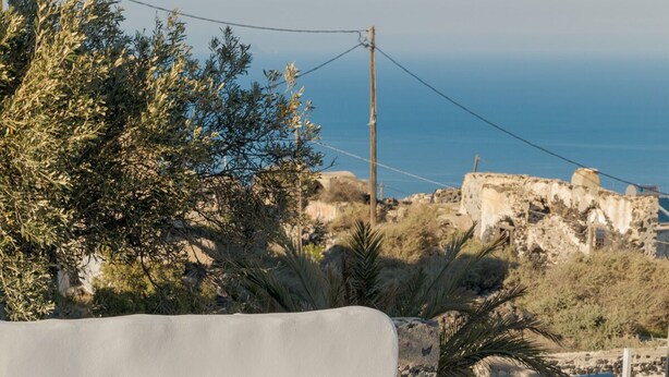 A modern outdoor seating area with a white sofa, a small round table, and a lounge chair. - Crown Of Fira (Santorini)