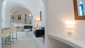 A modern, minimalist room with a curved white wall, a bed with striped bedding, a small round table, and a chair. - Crown Of Fira (Santorini)