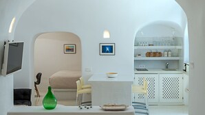 A minimalist room with a white color scheme, a small table with chairs, a green bottle, and a framed picture on the wall. - Crown Of Fira (Santorini)