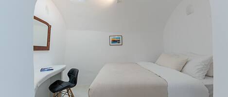 A bedroom with a bed, a desk, a chair, a mirror, and a picture on the wall.
